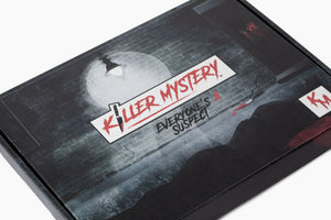 Pictured is an image of the Killer Mystery game box. The logo consists of a creepy font spelled out "killer mystery", with the "I" in Killer replaced by a bloody knife. Underneath the main logo is the tagline "Everyone's a suspect". The image is a back alley type scene  in which a street lamp shines down over a brick wall and silhouette of a body encapsulated  by a pool of blood, complete with bloody hand prints on a nearby door. 